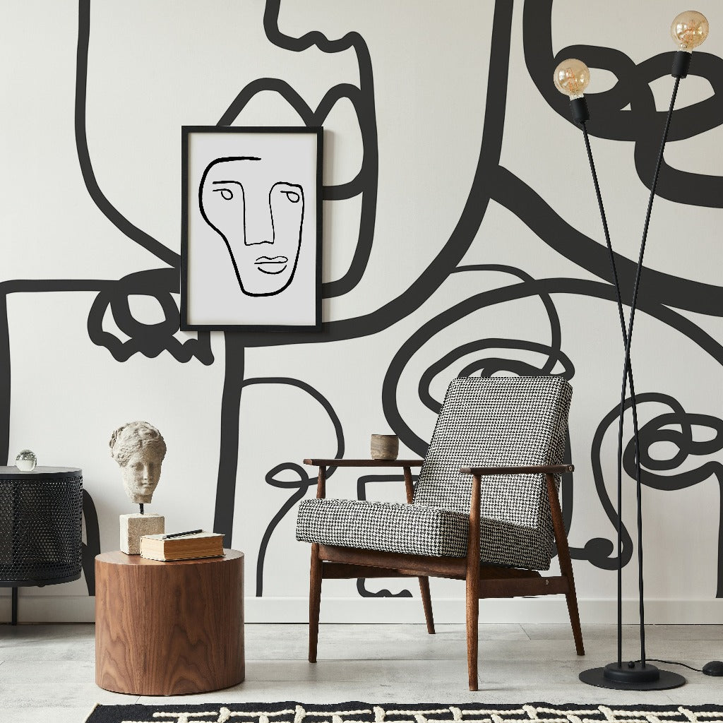 A modern living room with a Decor2Go Wallpaper Mural on the wall, a framed minimalist face artwork, a houndstooth armchair, a side table with books, and a minimalist design sculpture.