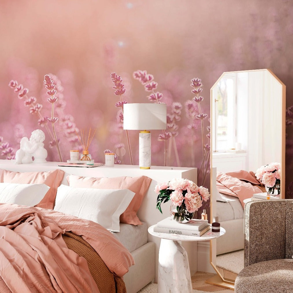 A cozy bedroom featuring soft pink bedding, a pink wall with a Field of Dreams Wallpaper Mural from Decor2Go Wallpaper Mural, a stylish lamp on a bedside table, fresh flowers in vases, and an elegant mirror.