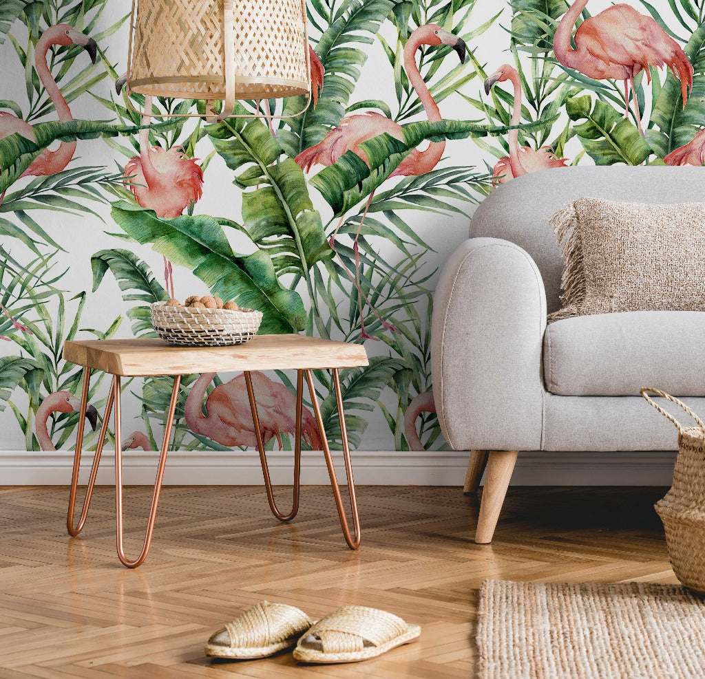 A cozy living room corner with a gray sofa, a wooden table with copper legs, Decor2Go Wallpaper Mural showcasing flamingos and green foliage, a straw hat, and two woven baskets on a textured rug.
