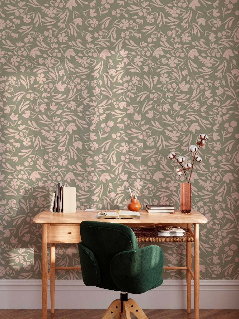 A cozy home office setup with a wooden desk and a green upholstered chair, facing a wall with Floral Bliss Wallpaper Mural from Decor2Go Wallpaper Mural, featuring pink flowers. The desk holds books, a potted plant, and some stationery.
