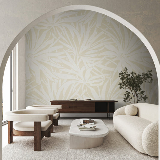 A modern living room with cream armchairs, a curved sofa, wooden sideboard, minimalist coffee table, and York Wallcoverings' Floral Canopy Beige Wallpaper Mural on a feature wall, viewed through an arched doorway.