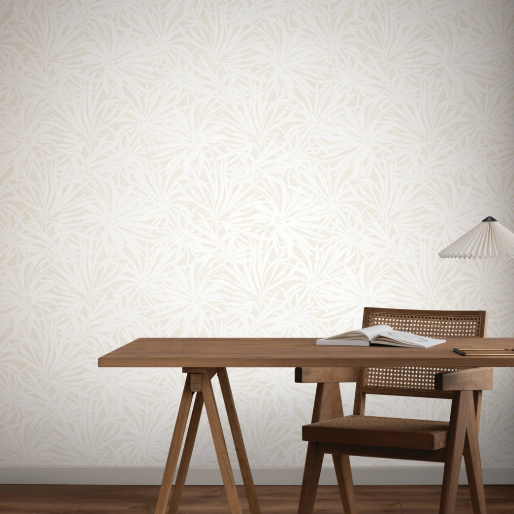 Home Office - A minimalist with a wooden desk and chair, an open book, and a modern white lamp. The background features York Wallcoverings’ Floral Canopy Cream Wallpaper (60 SqFt) with a light leafy pattern