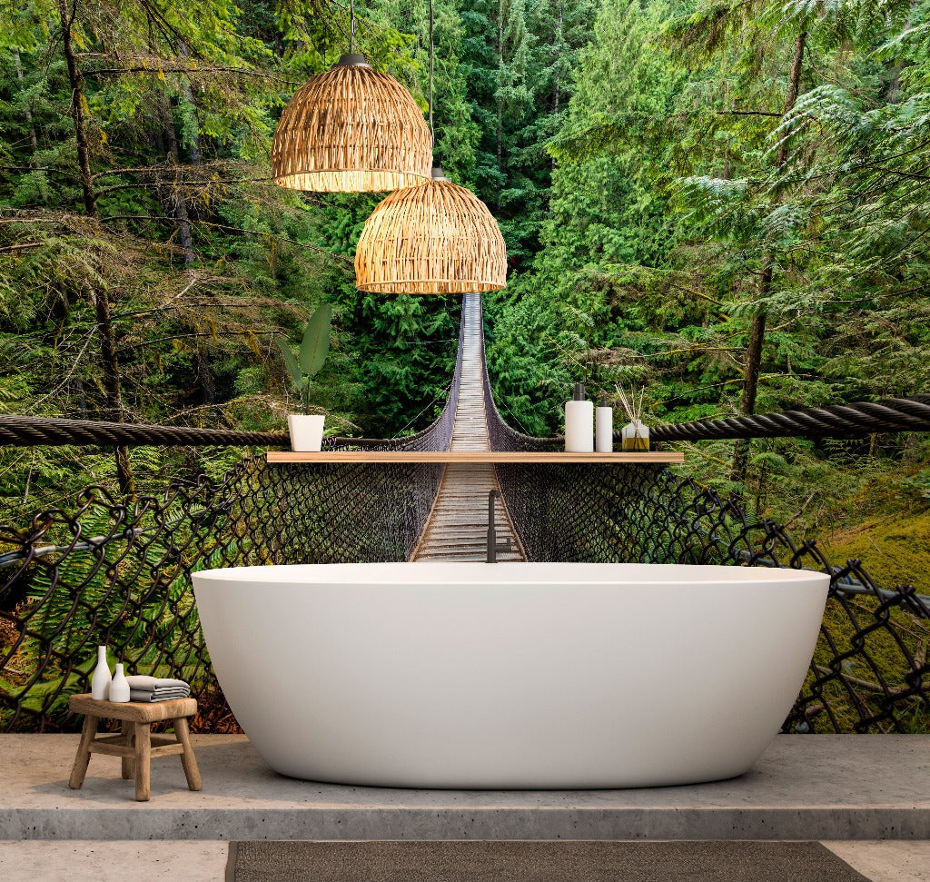 A luxurious freestanding bathtub set on a concrete floor with a backdrop of a custom Decor2Go Wallpaper Mural depicting a lush green forest and a wooden suspension bridge. Above the tub hang two woven pendant lights, enhancing