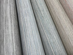 A close-up view of five fabric rolls displayed vertically, showcasing a spectrum of colors including shades of gray, blue, and beige. The fabrics have a subtle textured pattern, giving them a slightly woven appearance reminiscent of Fountain Grass Smokey Blue Wallpaper Blue (60 Sq.Ft.) by York Wallcoverings for a natural aesthetic.