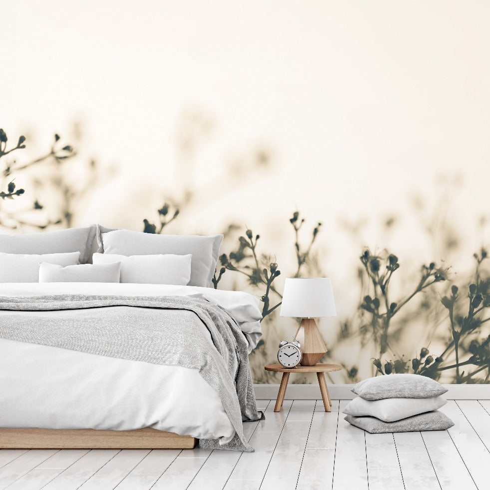 A serene bedroom featuring a neatly made bed with gray and white bedding, a wooden bedside table with a lamp and clock, set against a soft beige wall adorned with Decor2Go Wallpaper Mural's Fragile Flowers Wallpaper Mural.