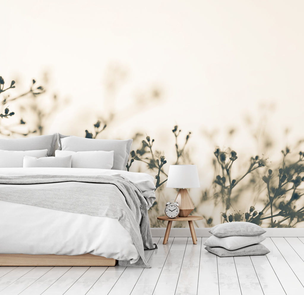 A serene bedroom featuring a neatly made bed with gray and white bedding, a wooden bedside table with a lamp and clock, set against a soft beige wall adorned with Decor2Go Wallpaper Mural's Fragile Flowers Wallpaper Mural.