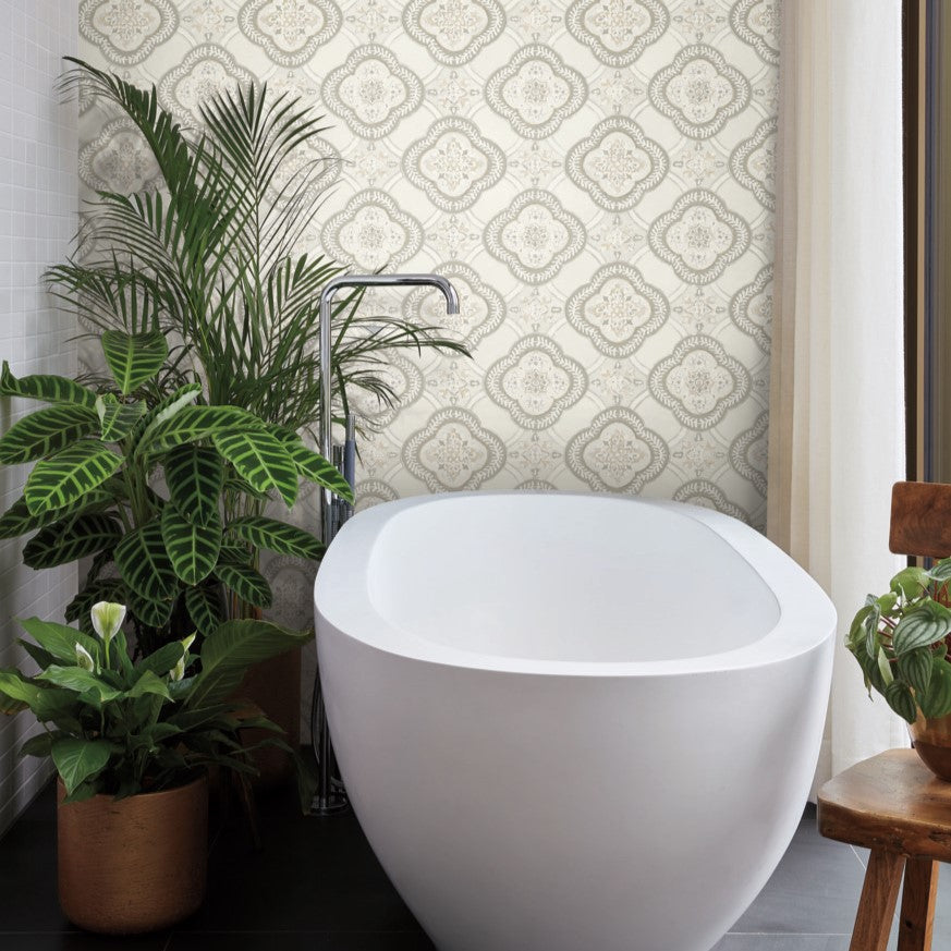 A modern bathroom exuding botanical elegance features a white freestanding bathtub in front of York Wallcoverings' Garden Trellis Cobalt Wallpaper Blue (60 Sq.Ft.). To the left of the tub, several green potted plants, including a peace lily and a large leafy plant, flourish alongside a wooden chair and a glass window.