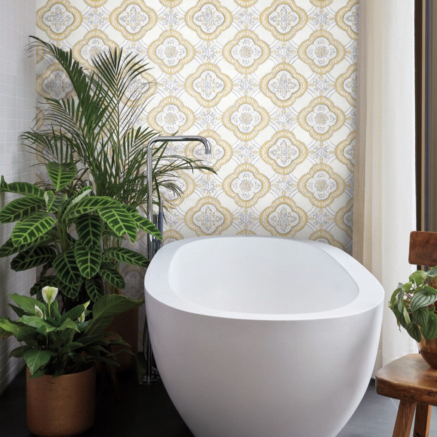 A modern bathroom with a white freestanding tub placed in front of a wall adorned with York Wallcoverings' Garden Trellis Cobalt Wallpaper Blue (60 Sq.Ft.) that echoes a garden trellis design. Several potted plants, including tall and leafy ones, enhance the space's botanical elegance. A wooden chair sits on the right.