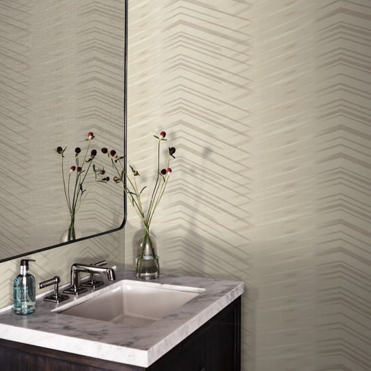 A stylish bathroom corner featuring a marble sink, modern faucet, and a mirror reflecting a vase with red flowers. The walls are adorned with York Wallcoverings' Glistening Chevron Wallpaper Blonde (56 sq.ft.) showcasing a subtle geometric pattern.