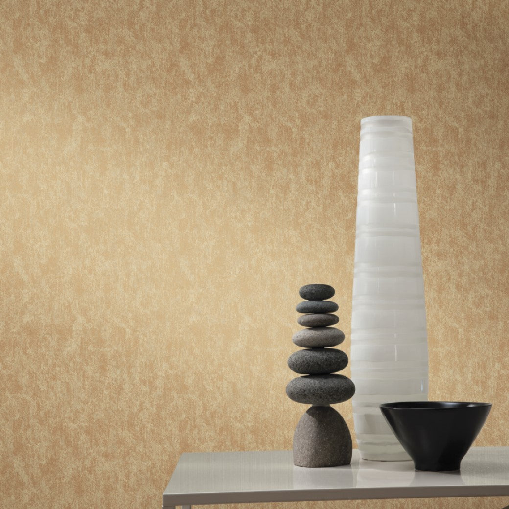 A minimalist setup with a tall white vase, smooth gray stones, and a small black bowl on a simple white table against a textured beige wall embodies the elegance of York Wallcoverings' Gold on Taupe Shimmering Patina Wallpaper.