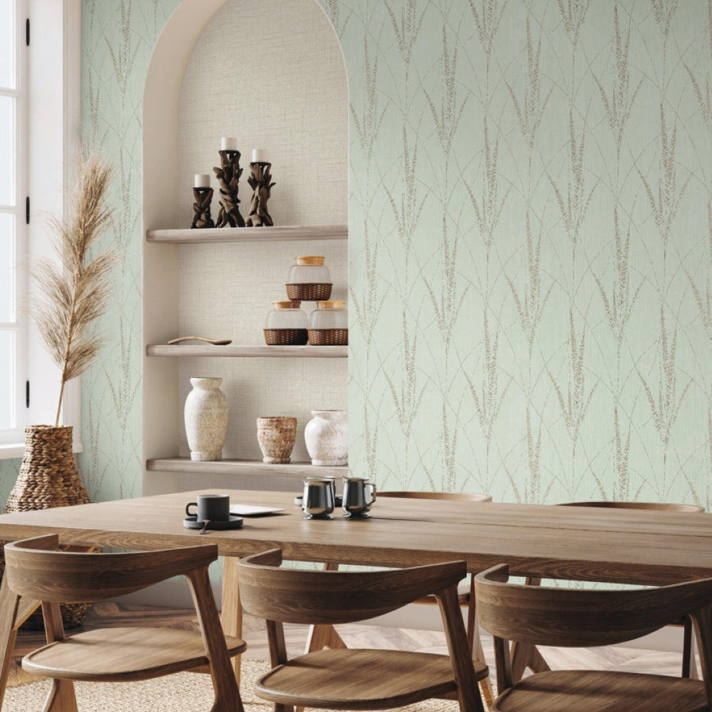 A modern dining room includes a wooden table, four chairs, and an arched shelf with vases and candles. Graceful Willow Lagoon Wallpaper by York Wallcoverings in light green with a leafy pattern adds charm as sunlight enters from the left window.