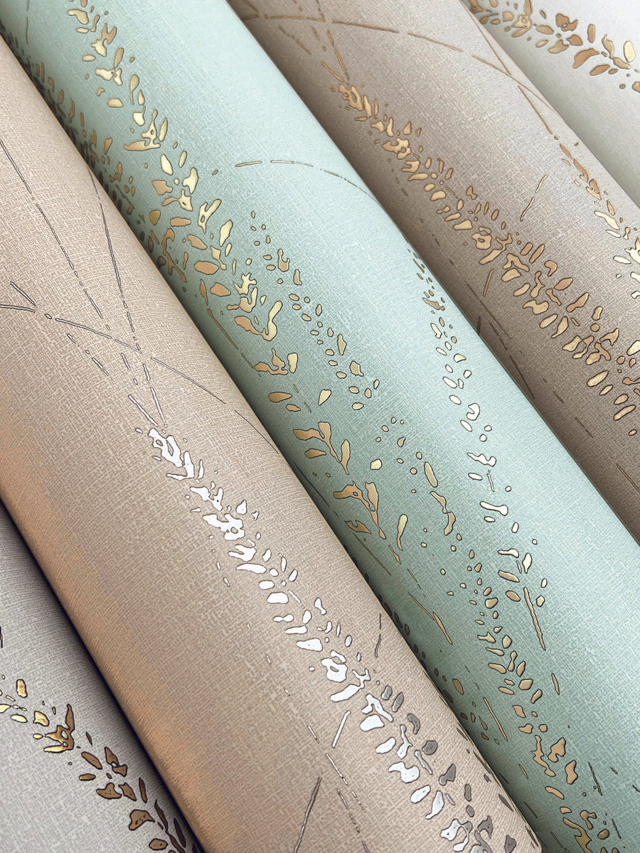 Close-up of York Wallcoverings Graceful Willow Pale Straw Wallpaper, showing rolled fabric with metallic gold leaf and branch patterns on pastel beige and light blue, evoking an elegant willow motif.