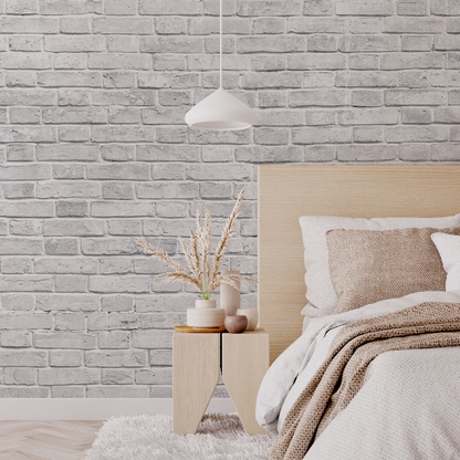 A cozy bedroom corner featuring a neatly made bed with a beige headboard and knit throw, a wooden side table with a vase of dried plants, under a pendant light against the Decor2Go Wallpaper Mural background.