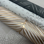 Three rolls of decorative wallpaper from the Modern Metals Collection: a silver geometric pattern on a dark background, York Wallcoverings' Grey & Gold Luminous Leaves, and a shiny abstract design on beige.