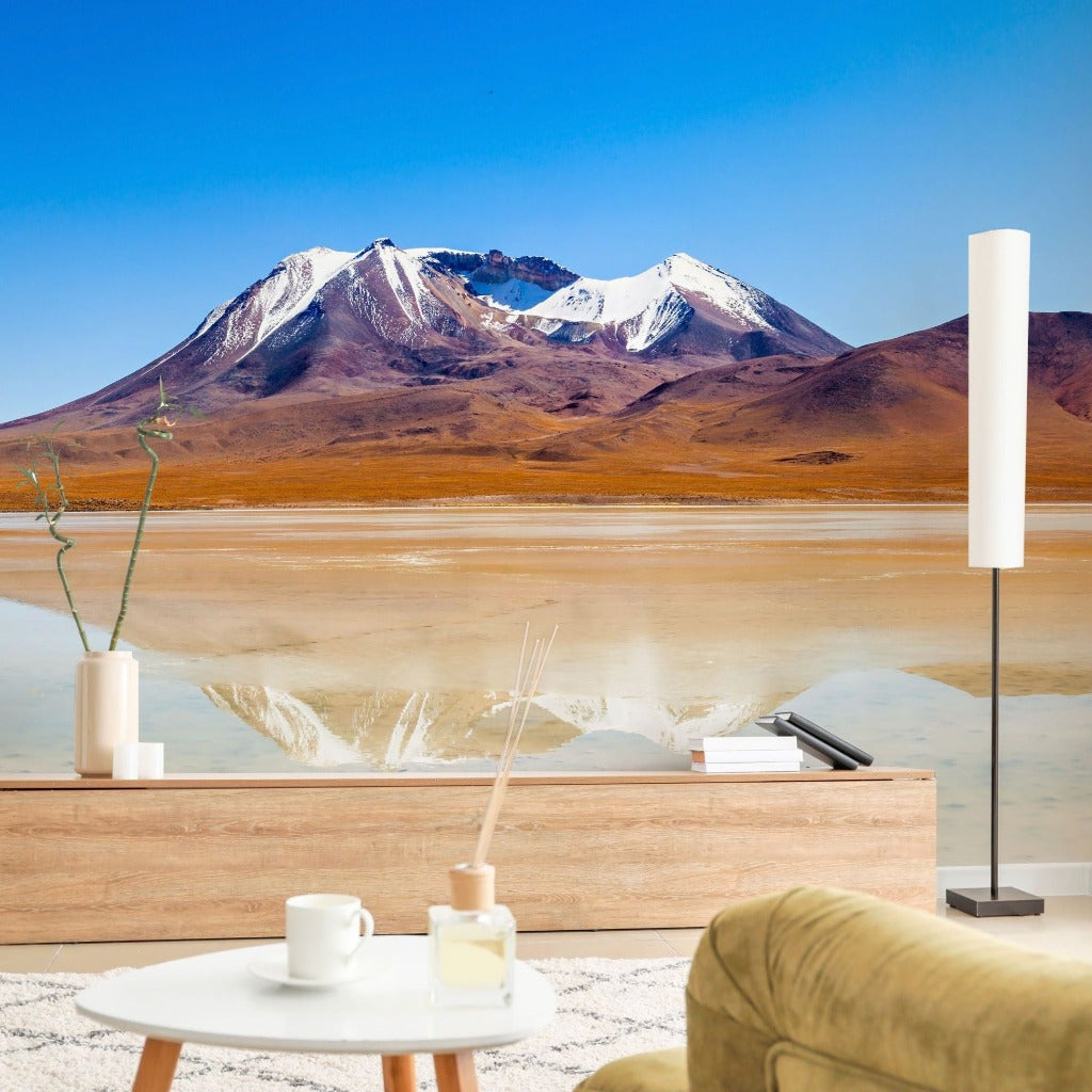 A tranquil living room overlooking a stunning landscape with snow-capped mountains and a reflective lake, featuring a modern wooden console, cozy seating, and the Decor2Go Wallpaper Mural.
