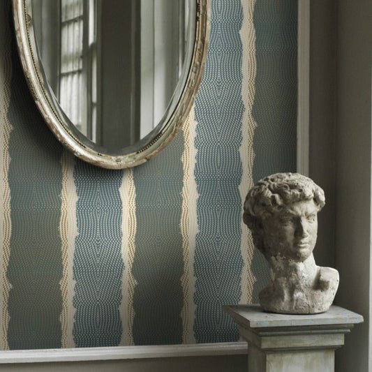 An ornate round mirror hangs on a wall adorned with Indigenous Wallpaper - Teal (56 SqFt) by York Wallcoverings. In front of the wall is a classical-style marble bust placed on a pedestal. The scene is illuminated by natural light from a nearby window.