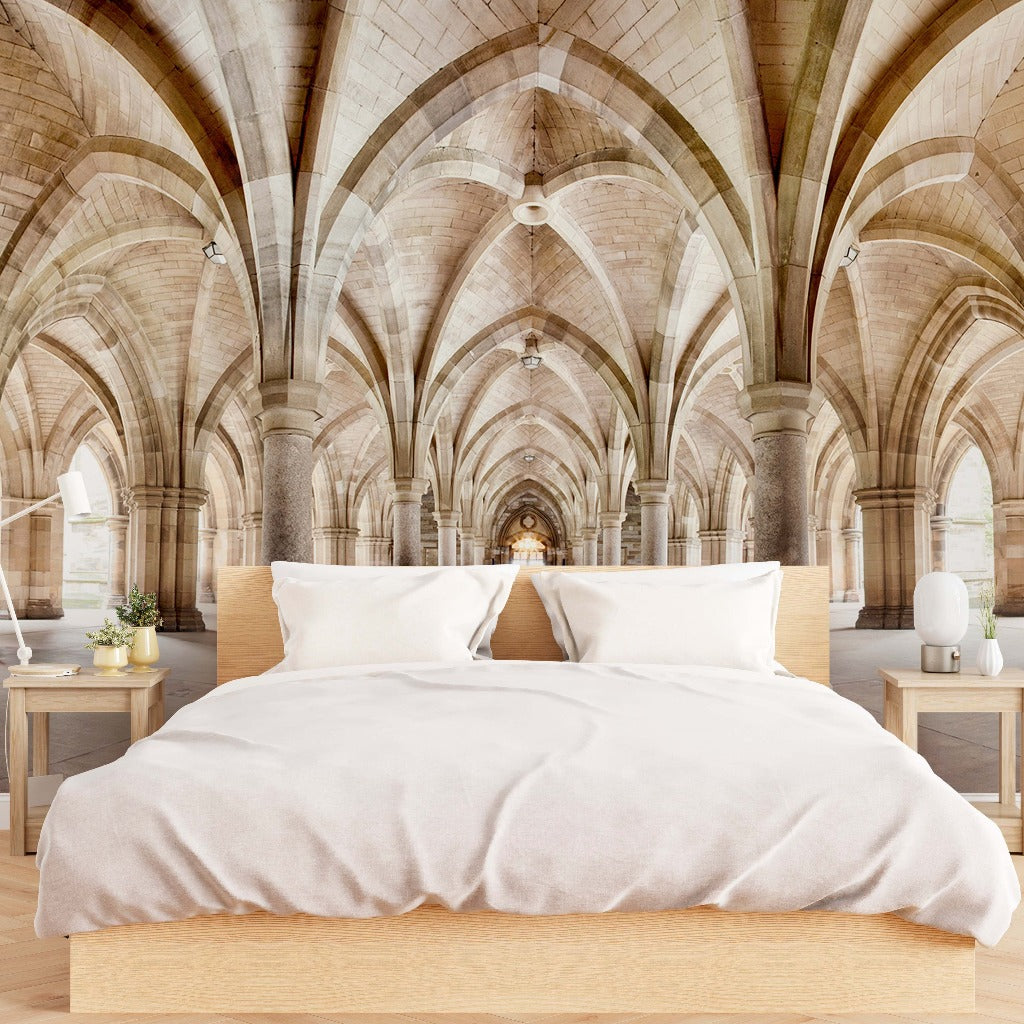 A modern bed with beige bedding set up in the Glasgow University cloister, featuring high arched stone ceilings and pillars, blending contemporary living with historical architecture with Decor2Go Wallpaper Mural's Infinite Paths Wallpaper Mural.