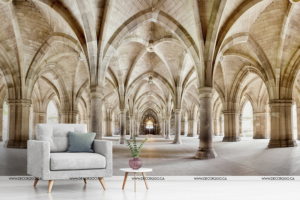 A stylized image combining a modern living room setup with a grey armchair and side table inside Glasgow University cloister, featuring arched ceilings and Gothic architectural elements by Decor2Go Wallpaper Mural's Infinite Paths Wallpaper Mural.