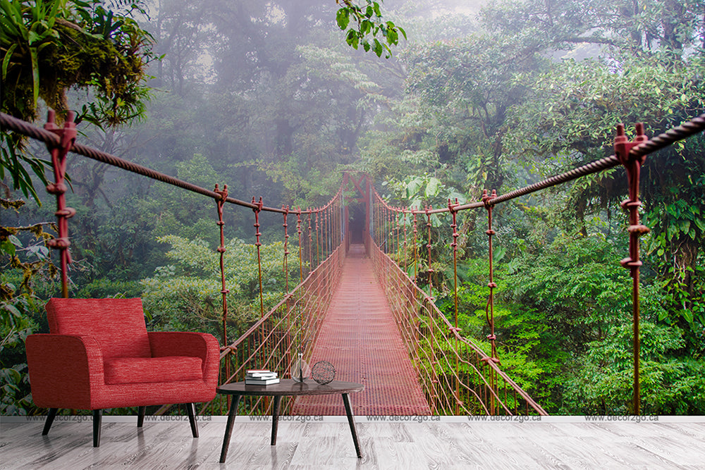 A surreal image of a red armchair and a small table with books and a cup juxtaposed with a scene of a misty suspension bridge in a lush forest, suggesting a blend of Into the Forest Wallpaper Mural from Decor2Go Wallpaper Mural decor.