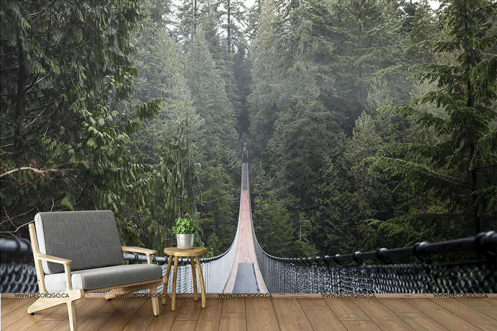 An artistic rendering of a modern armchair and side table on a wooden deck, overlooking a suspension bridge extending into a dense, fog-covered forest Decor2Go Wallpaper Mural.