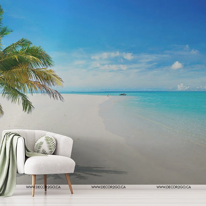 A serene beach scene with a stylish chair adorned with a green cushion, a striped blanket hanging over, and Island in the Sun Wallpaper Mural beside it, overlooking a calm turquoise sea and clear sky.