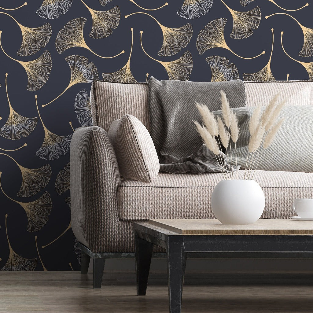 A cozy living room corner featuring an elegant beige sofa with a dark textured throw and a white vase with dried plants on a black coffee table. The room has Decor2Go Wallpaper Mural featuring Japanese Flowers design and metallic gold accents.