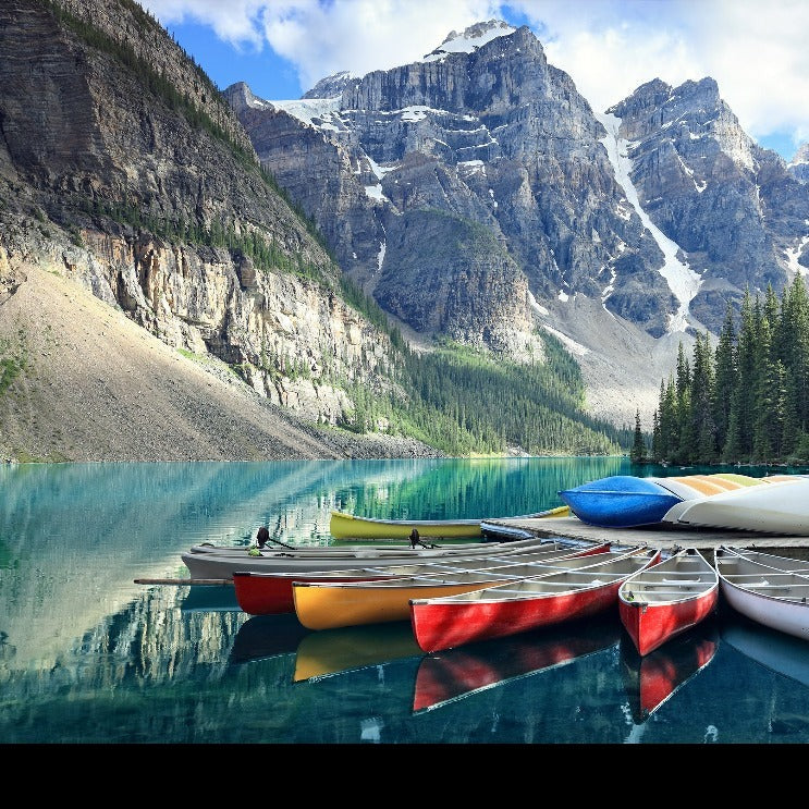 Colorful canoes on a dock at a crystal-clear lake with towering, snow-capped mountains and dense pine trees in the background, perfectly captured in the Decor2Go Wallpaper Mural.