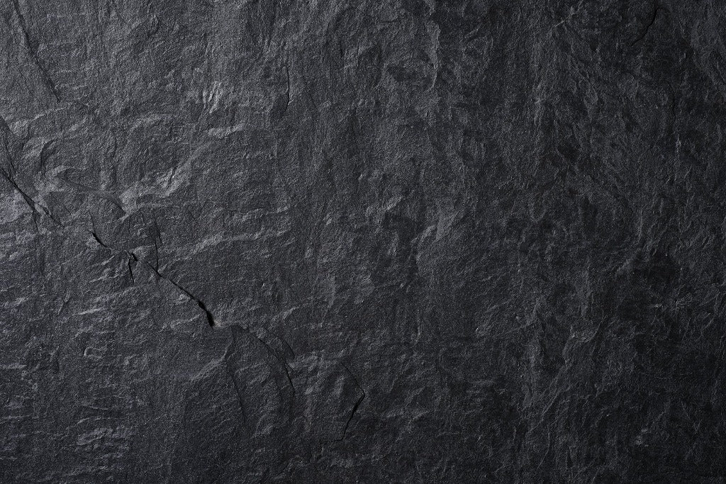 Close-up photo of a dark, textured stone surface with visible natural patterns and a few small, subtle cracks, ideal for a Decor2Go Wallpaper Mural Lava Rocks wallpaper design.