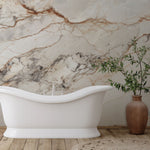 A modern bathroom interior featuring a sleek, freestanding white bathtub with elegant curves. Behind the tub is a wall adorned with the Light Brown Marble Wallpaper Mural by Decor2Go Wallpaper Mural in white, grey, and beige tones. A tall, brown ceramic vase with green leafy branches stands on the right side on a wooden floor.