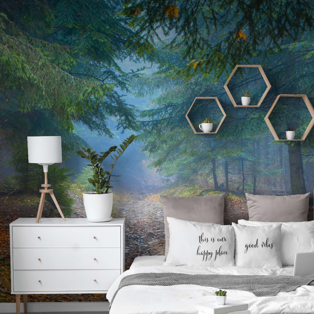 A stylish bedroom featuring the Decor2Go Wallpaper Mural "Magic Forest" with a scenic view of a misty forest path lined by emerald-hued trunks. The room includes a white dresser, modern lamp, geometric
