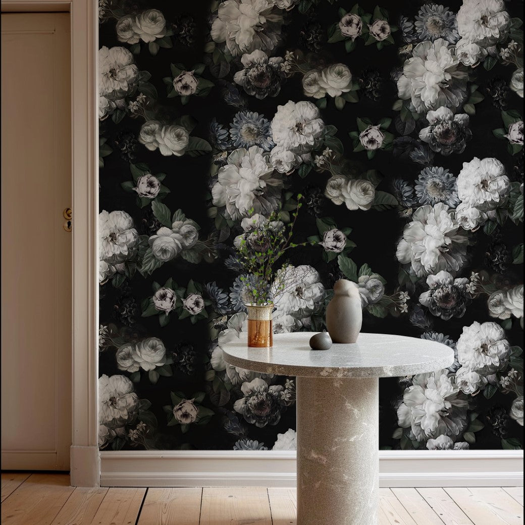 A round stone table with two vases is set on a wooden floor against the Decor2Go Midnight Bloom Floral Wallpaper Mural, featuring dark floral patterns of white and gray. A closed door can be seen on the left.