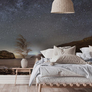 Bedroom - A serene bedroom with a Milky Way Galactic Coast Wallpaper Mural from Decor2Go Wallpaper Mural, featuring the Milky Way galaxy, with a cozy bed adorned with plush pillows and a gray blanket, a wicker pendant lamp above, and a side table.