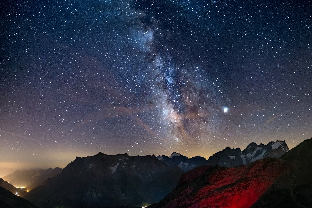 Stunning view of the Milky Way Wallpaper Mural over rugged mountain peaks, with one peak illuminated in red under a star-studded night sky.