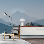 Living Room - A minimalist living room with a gray armchair, white sideboard, decorative objects, and a Misty Blue Mountains Wallpaper Mural by Decor2Go Wallpaper Mural on the feature wall. A floor lamp, magazine, and bird figure on the sideboard.