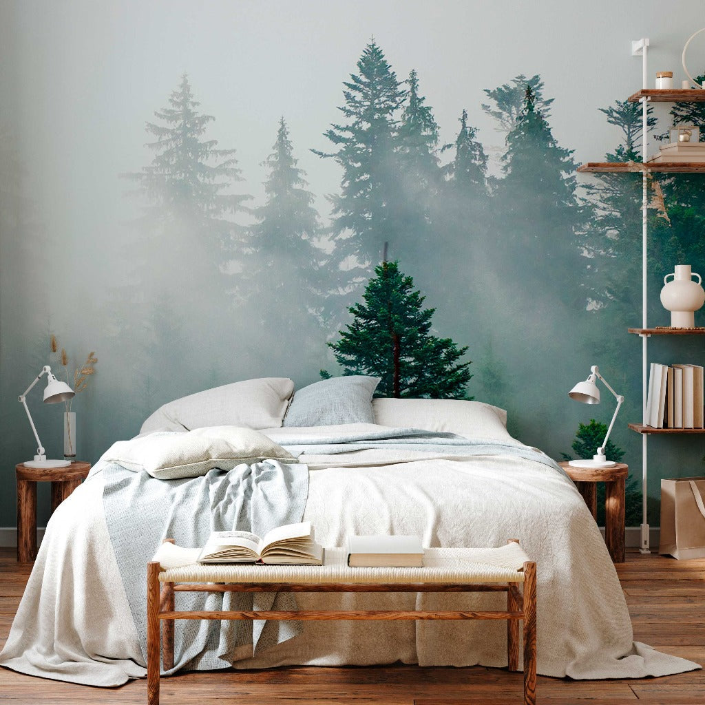 A serene bedroom with a Decor2Go Wallpaper Mural of a Misty Forest, featuring a neatly made bed, a wooden bench with an open book, and a side shelf with various decor items.