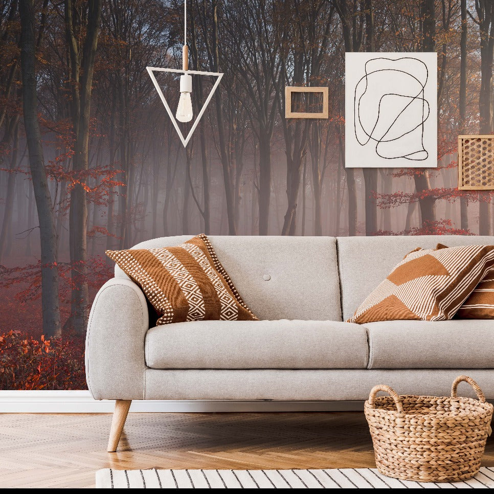 A modern living room with a gray sofa adorned with patterned cushions, a wicker basket, and abstract wall art, overlooking a Decor2Go Wallpaper Mural featuring the Misty Red Forest Wallpaper Mural.