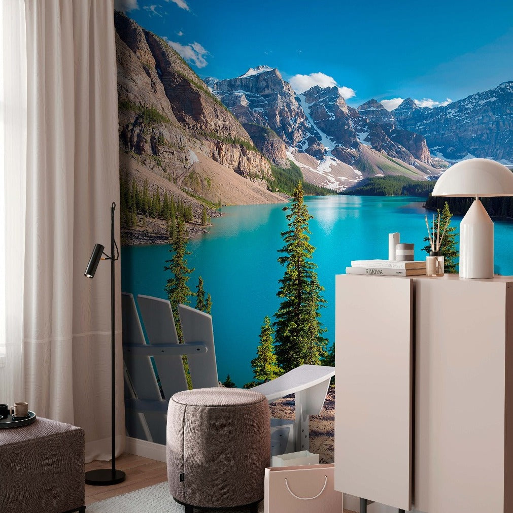 A cozy room with a large window featuring a wall-sized Decor2Go Wallpaper Mural. The room includes a gray chair, floor lamp, and small, modern furnishings.