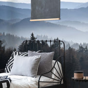 Bedroom - A cozy bedroom with a wrought iron bed adorned with patterned pillows, featuring a Decor2Go Wallpaper Mural, overlooking a foggy, tree-covered mountain landscape through large windows.