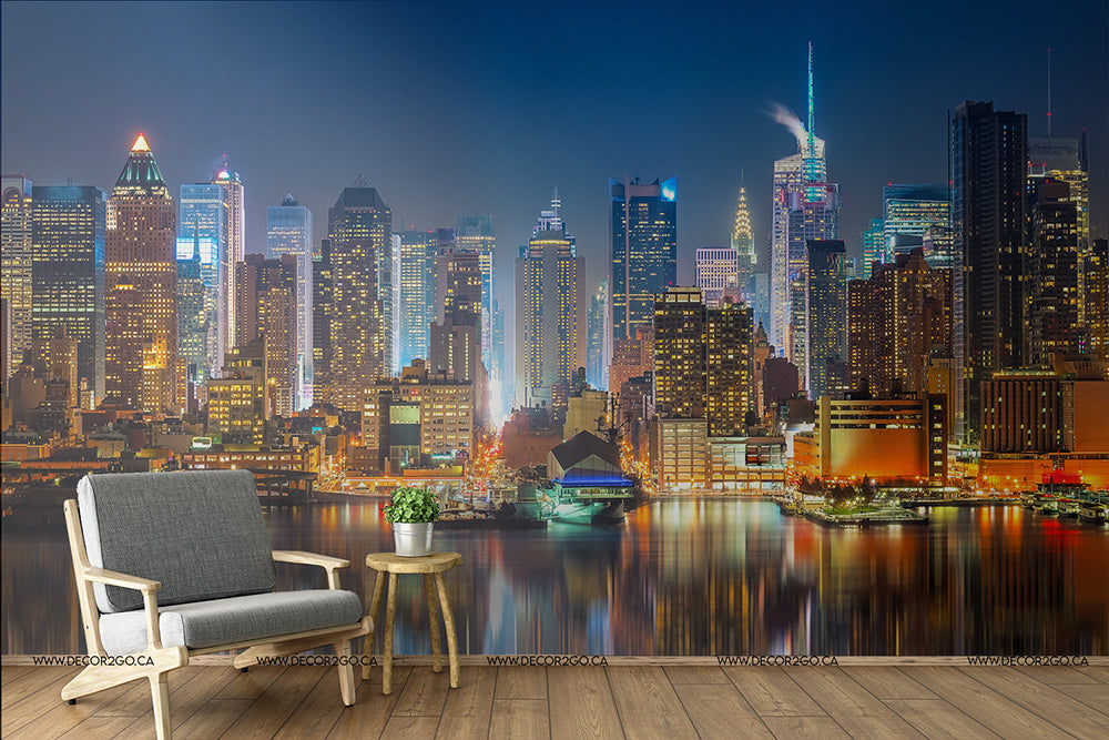 A surreal room with a Decor2Go Wallpaper Mural of the vibrant NYC skyline at night featuring illuminated skyscrapers, reflected in calm water, paired with a modern armchair and a small wooden side table.