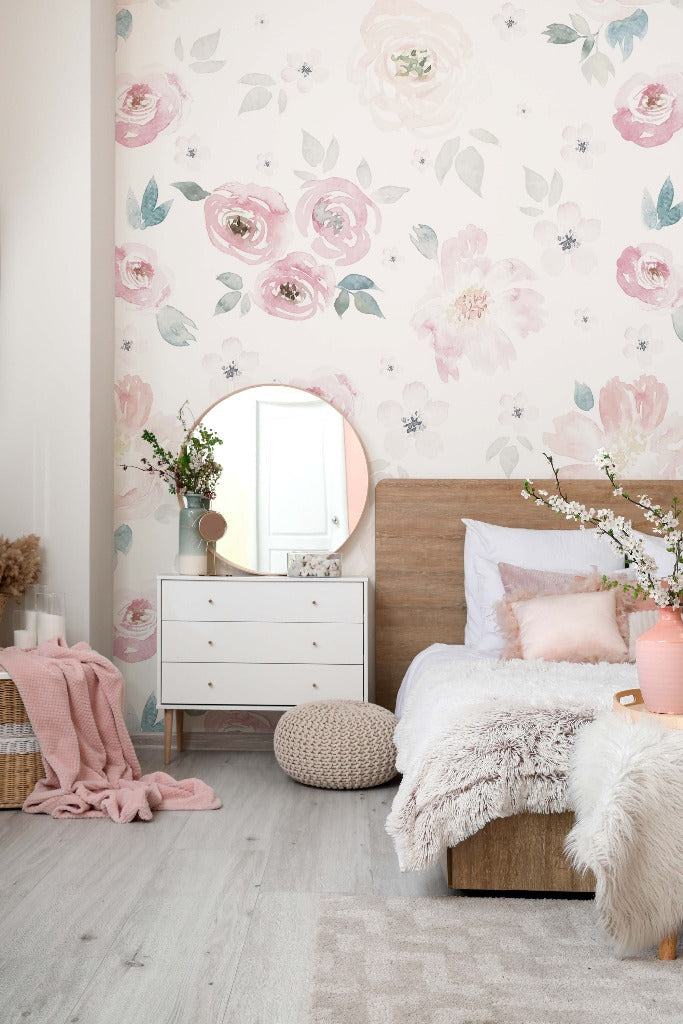 A cozy bedroom featuring a wooden bed with white and pink bedding, a white dresser with a round mirror, Decor2Go Wallpaper Mural, and decorative flowers. Soft pink accents and textures create a warm atmosphere.