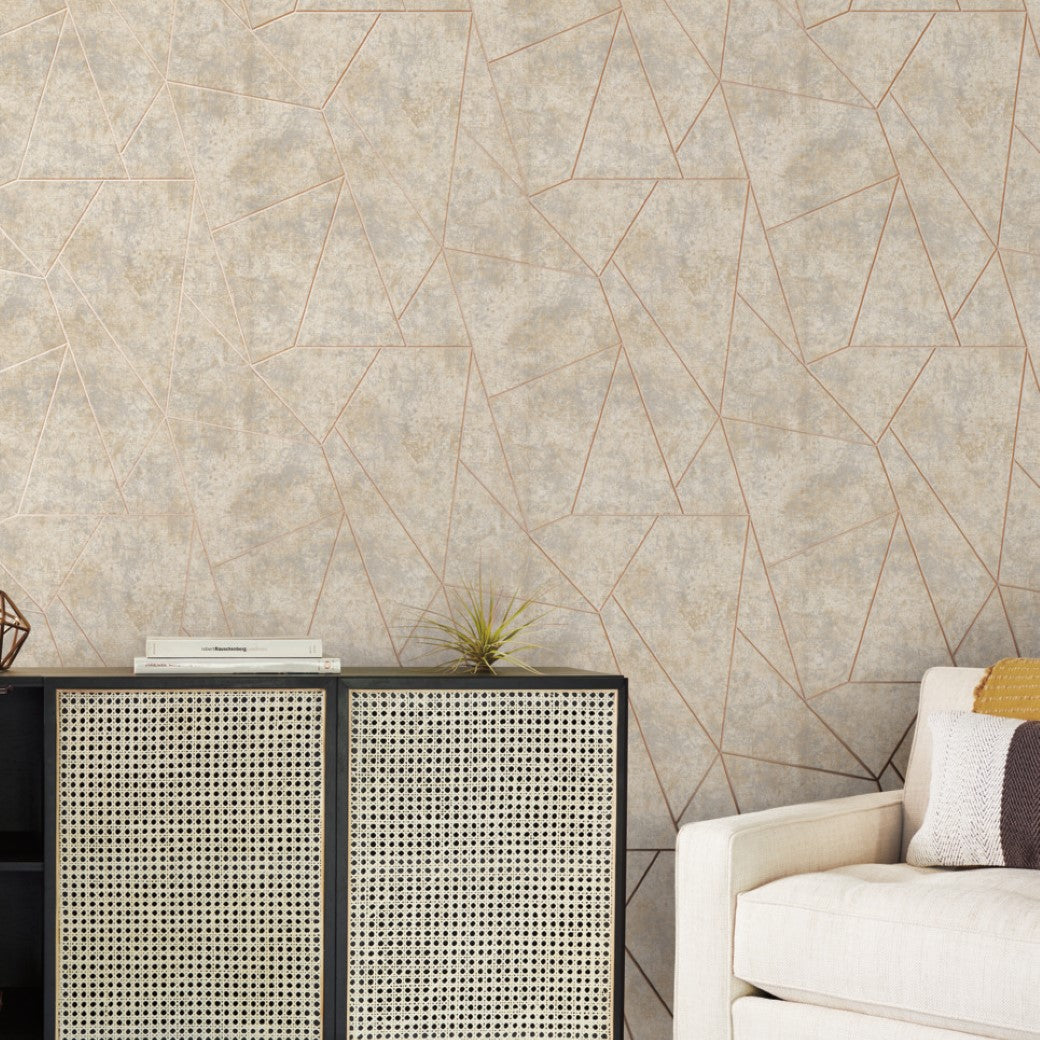 A modern living room features York Wallcoverings' Neutral & Gold Nazca Wallpaper. A light sofa with a striped pillow sits on the right, while a black console with a rattan front and metallic finish stands against the wall, adorned with a small plant.