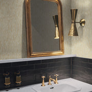 Bathroom - A with a gold-framed mirror and brass wall light above a white sink featuring Modern Metals accents. The sink includes gold faucets on black-tiled backsplash, and soap dispensers rest on a spa blue with silver metallic countertop. The walls are covered in York Wallcoverings' Spa & Silver Metallic Cascade Wallpaper