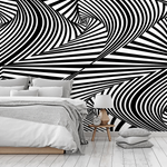 A modern bedroom with a striking black and white Decor2Go Optical Illusion Wallpaper Mural design, featuring a minimalist bed with gray bedding, and a small wooden bedside table with a lamp and clock.