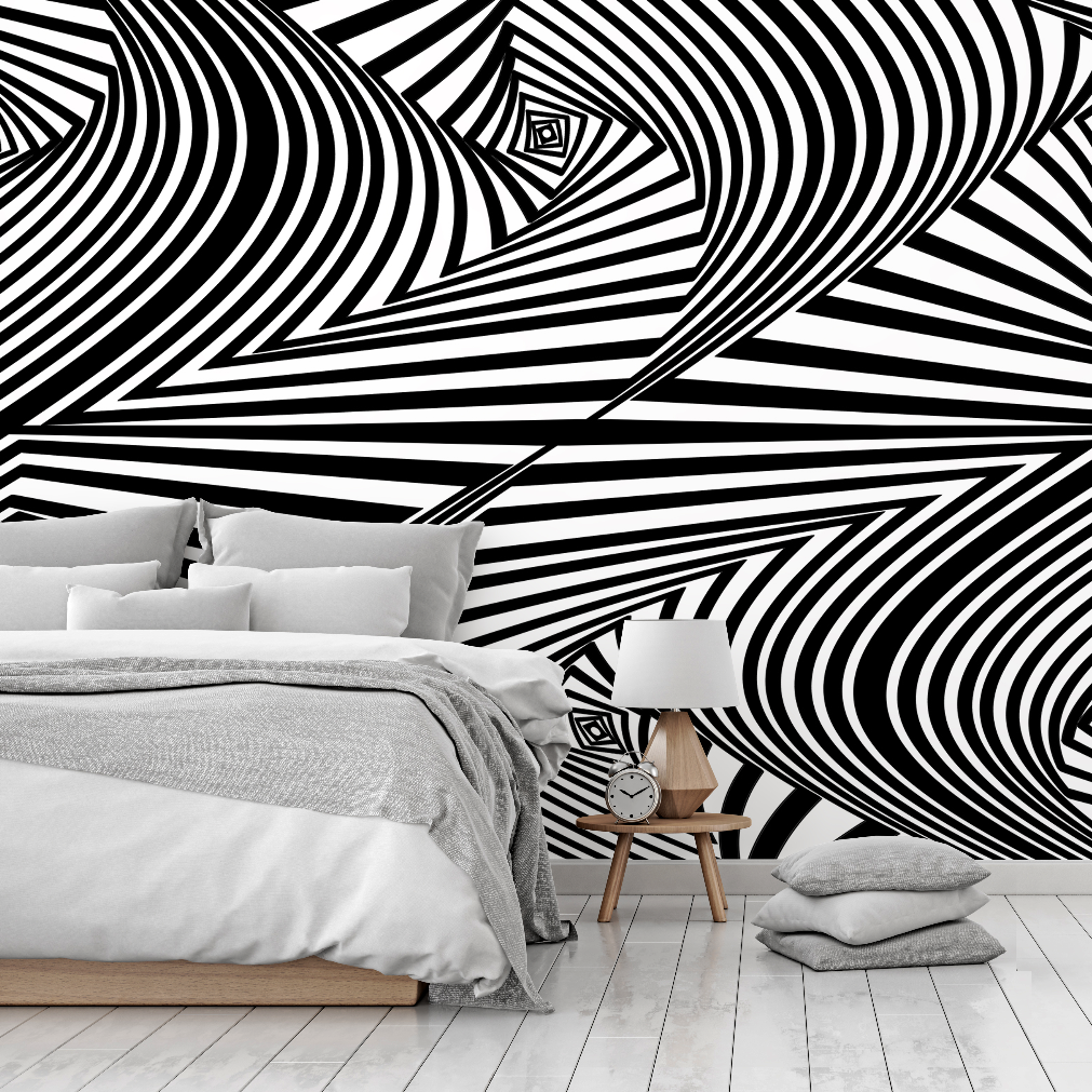 A modern bedroom with a striking black and white Decor2Go Optical Illusion Wallpaper Mural design, featuring a minimalist bed with gray bedding, and a small wooden bedside table with a lamp and clock.