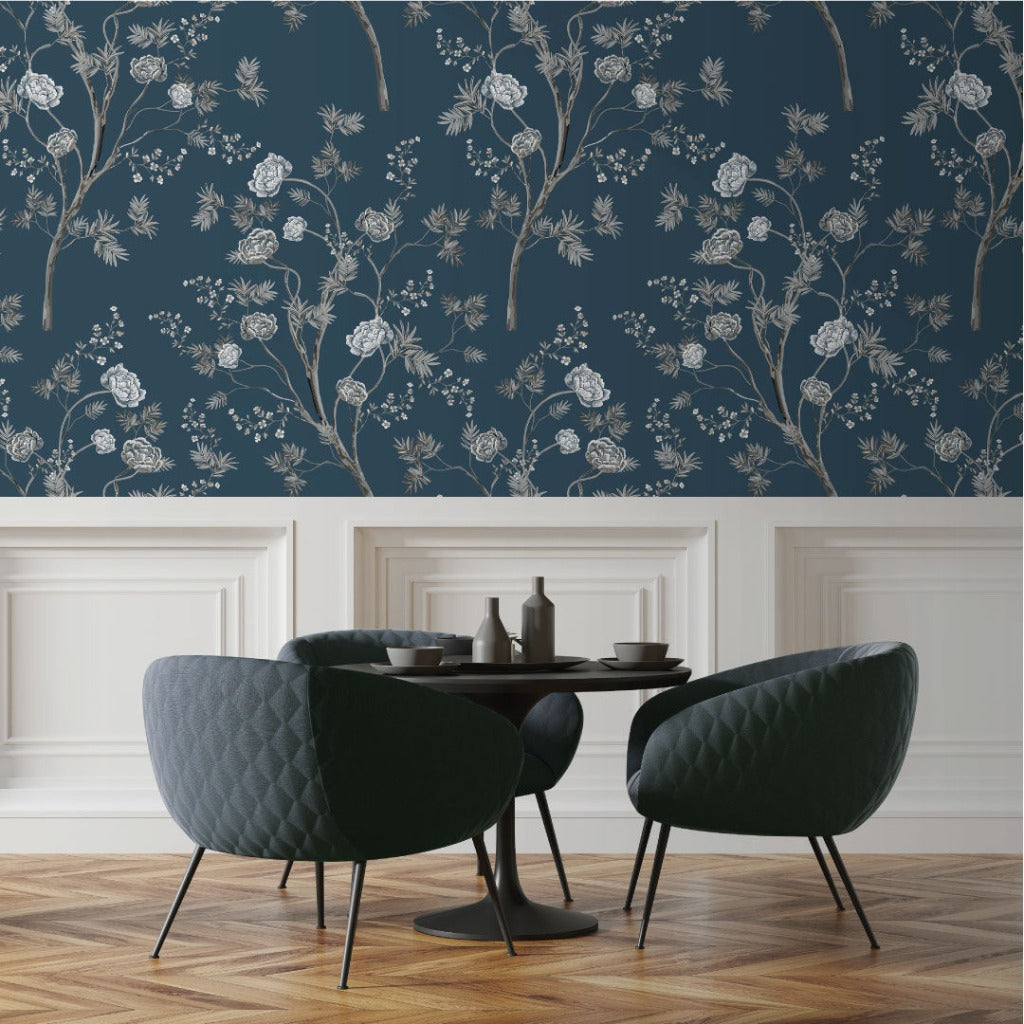 A dining area featuring two dark green, quilted chairs and a round table, set against a dark blue wall with elegant Decor2Go Oriental Garden Wallpaper Mural and white wainscoting.