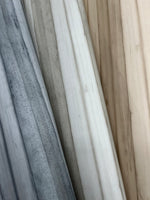 A close-up of several wooden planks arranged side by side. The planks show a range of colors from gray, white, and light brown, highlighting the natural wood grain and texture. The surface appears smooth with visible lines and imperfections, reminiscent of the easy installation and removal of Pandora Leaf Oak Wallpaper Brown (60 Sq.Ft.) by York Wallcoverings.