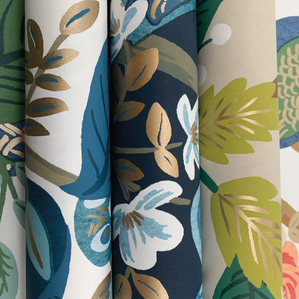 Four rolls of York's Periwinkle Peacock Wallpaper showcase floral Chinoiserie-inspired designs with leaves and flowers in blue, green, gold, and white on varied backgrounds. Each roll covers 60 SqFt with unique botanical patterns.