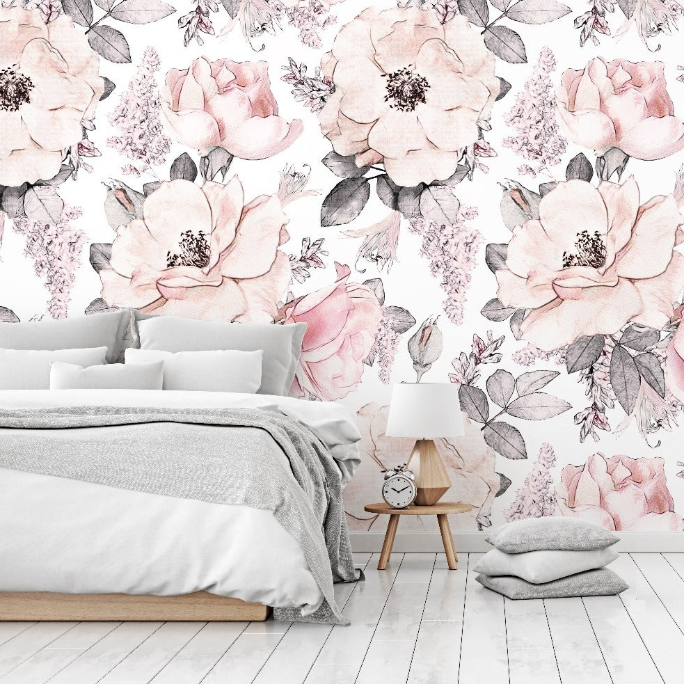 A bright bedroom with light wood floors and a wall covered in Decor2Go Wallpaper Mural featuring pink and white flowers. A simple bed with gray bedding and a wooden bedside table with a lamp.