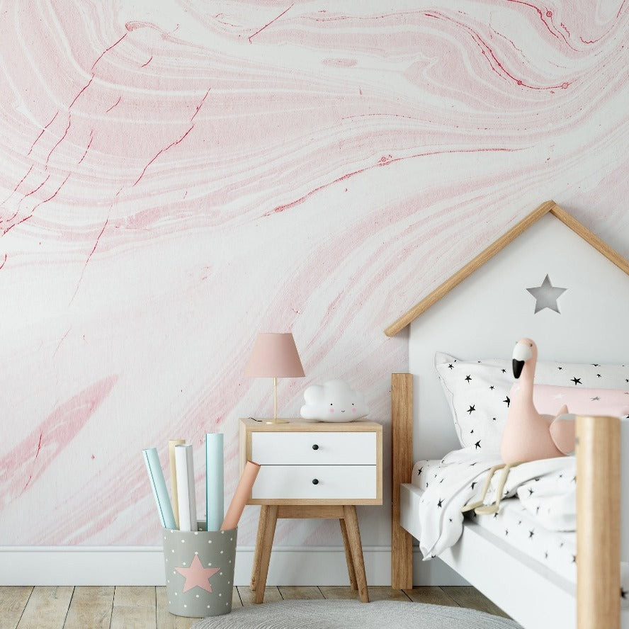 A cozy children's bedroom corner with a Decor2Go Wallpaper Mural pink marble wallpaper, a small wooden bed shaped like a house with star decor, a white nightstand, a pink lamp, and a container with colorful rolled papers.