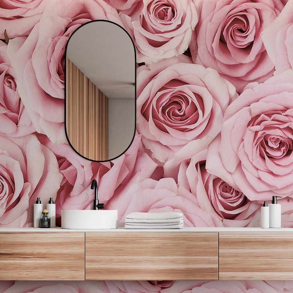 A stylish bathroom featuring a feature wall covered in large Pink Paradise Wallpaper Mural from Decor2Go Wallpaper Mural with a wooden vanity, white basin, oval mirror, and neatly arranged toiletries and towels.